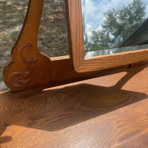 May include: A vintage wooden vanity mirror with a beveled glass mirror and ornate carvings. The mirror is open and the wood is a rich brown color.