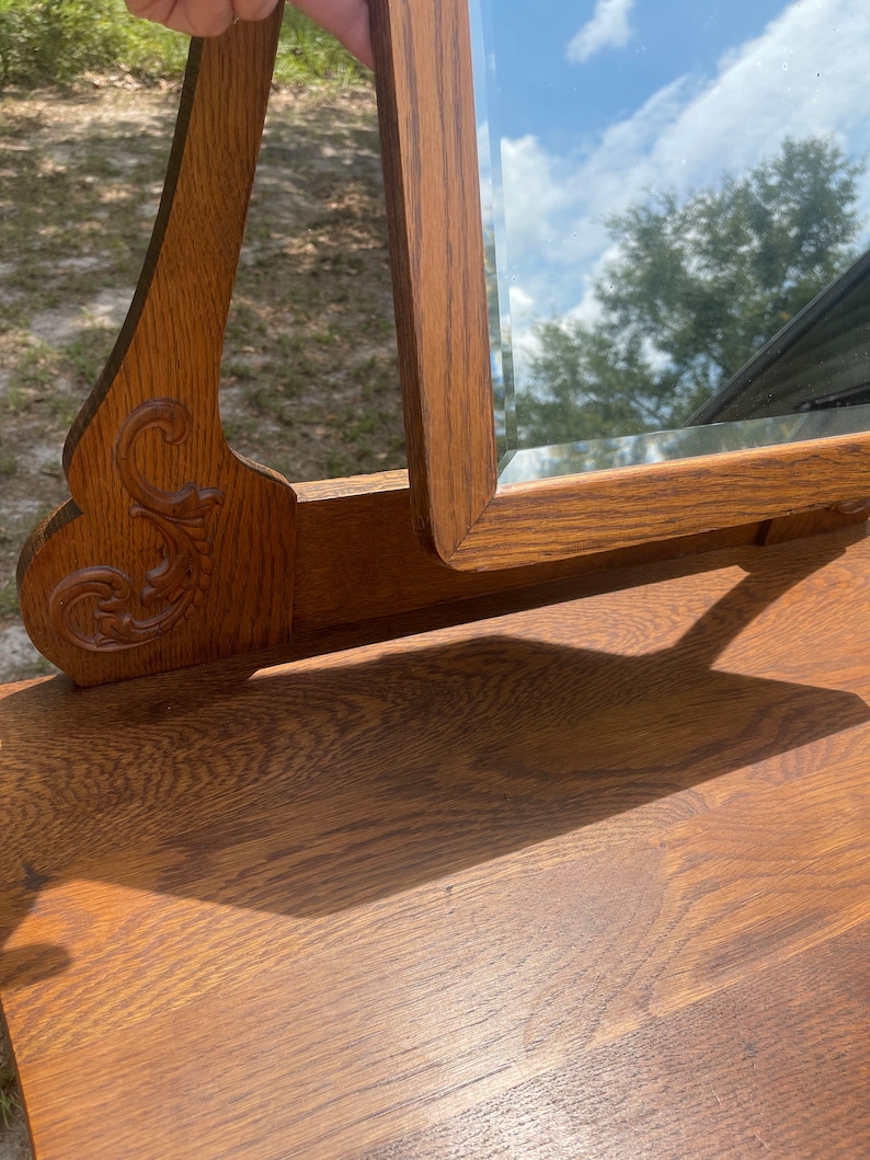 May include: A vintage wooden vanity mirror with a beveled glass mirror and ornate carvings. The mirror is open and the wood is a rich brown color.