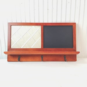 May include: A wooden wall organizer with a chalkboard, a corkboard, and three hooks. The organizer is stained a dark brown color.
