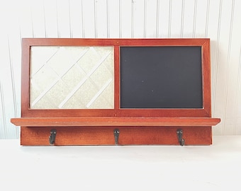 May include: A wooden wall organizer with a chalkboard, a corkboard, and three hooks. The organizer is stained a dark brown color.