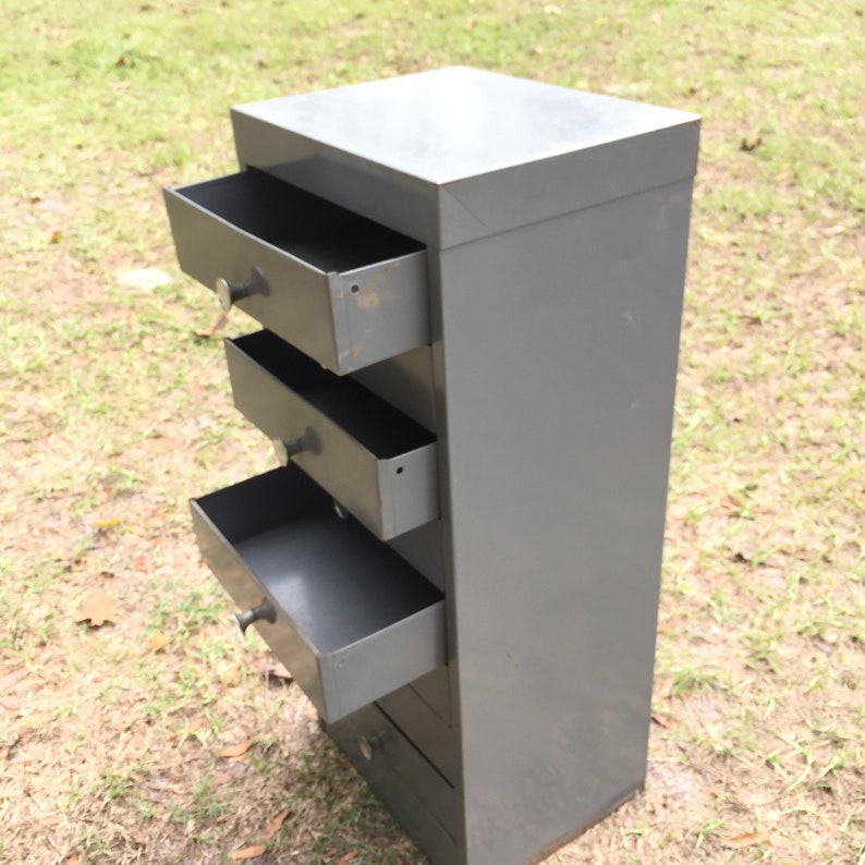 May include: A gray metal dresser with four drawers. The drawers are open and empty.