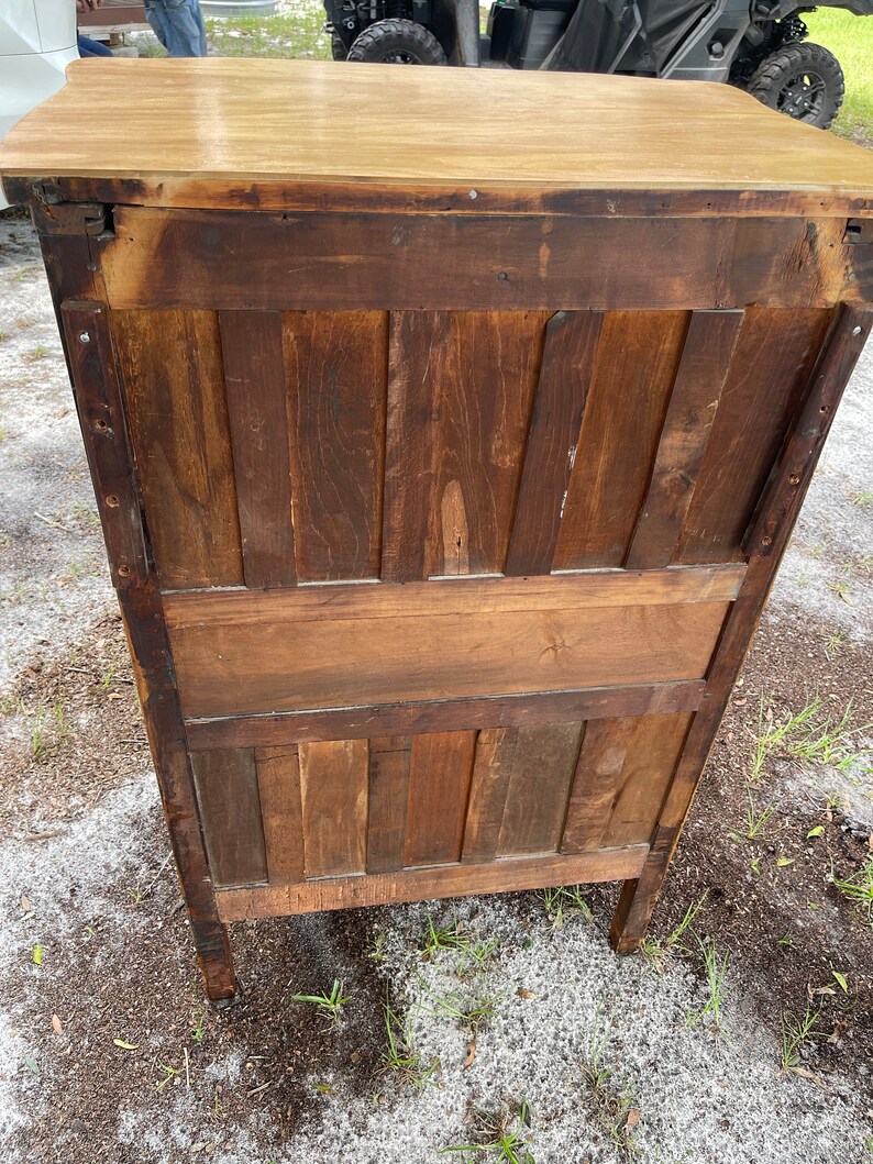 Puede incluir: La parte posterior de un armario de madera con una parte superior de color marr&oacute;n claro y un cuerpo de color marr&oacute;n oscuro. El armario tiene un dise&ntilde;o sencillo con paneles verticales y un estante.