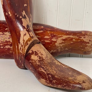 May include: A pair of vintage wooden shoe stretchers with a reddish-brown finish. The stretchers are worn and have a distressed look.