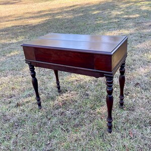 May include: A dark wood writing desk with a drop-down front and turned legs. The desk has a simple design and is in good condition.