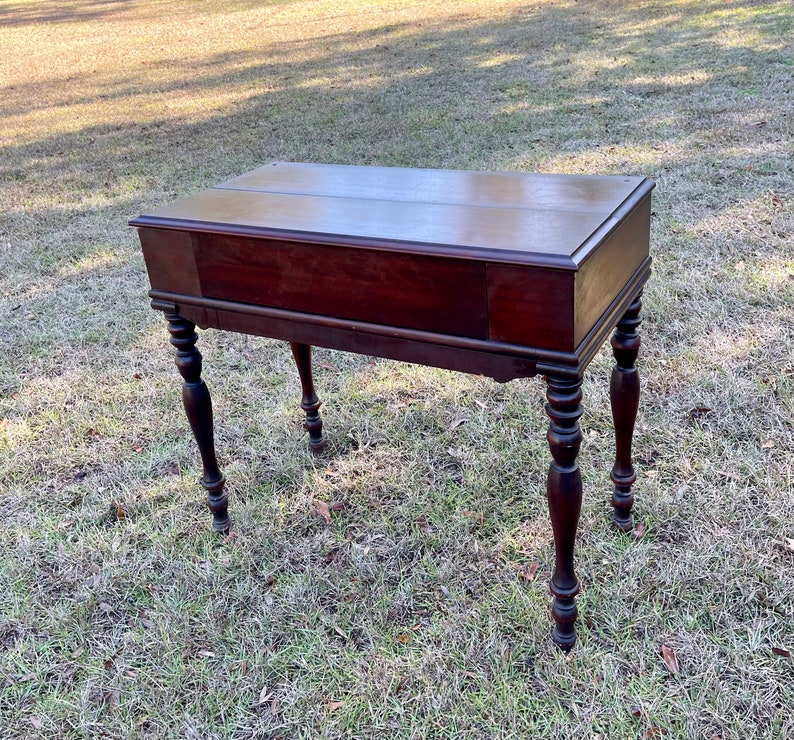 May include: A dark wood writing desk with a drop-down front and turned legs. The desk has a simple design and is in good condition.