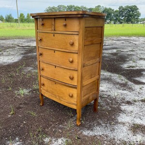 Puede incluir: Una c&oacute;moda de madera vintage con seis cajones y un frente curvo. La c&oacute;moda est&aacute; hecha de madera clara y tiene un acabado natural. Tiene patas torneadas y est&aacute; en buen estado.