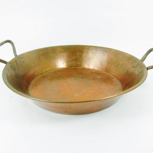 May include: A vintage copper pan with two handles. The pan has a hammered finish and is slightly tarnished.