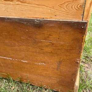 K&ouml;nnte beinhalten: Ein Holzschrank mit hellbrauner Oberfl&auml;che. Der Schrank hat eine einzelne T&uuml;r und ein unteres Regal. Der Schrank steht auf einem St&uuml;ck gr&uuml;nem Gras.