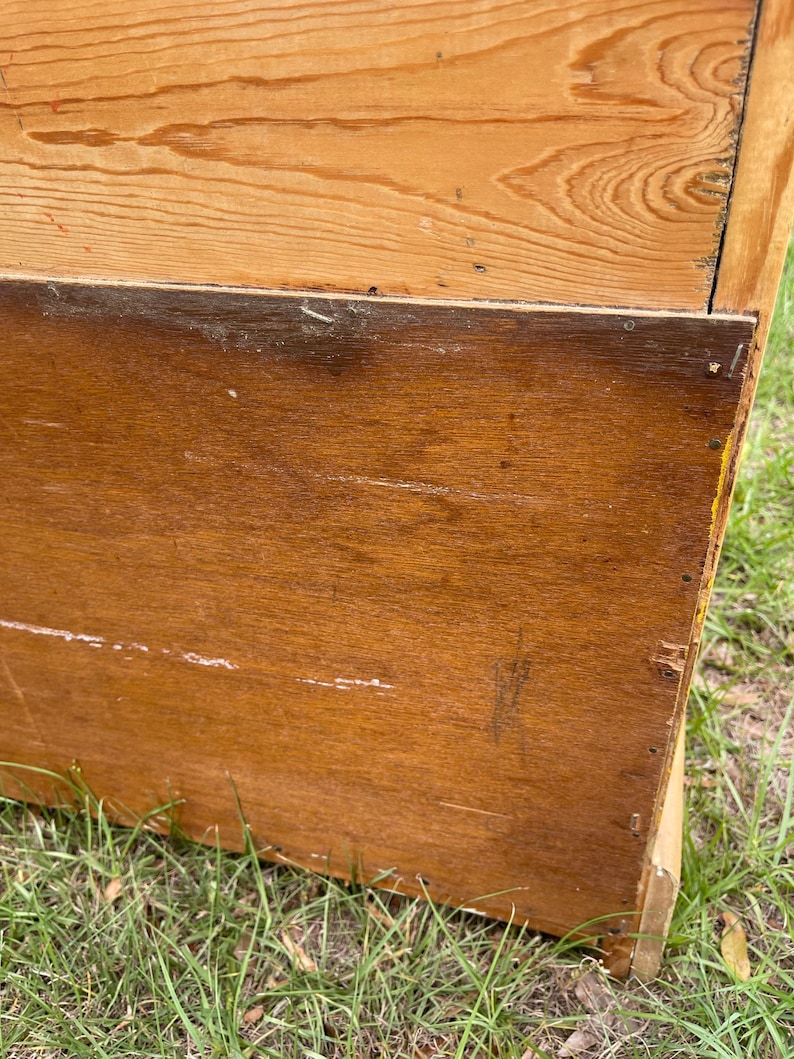 K&ouml;nnte beinhalten: Ein Holzschrank mit hellbrauner Oberfl&auml;che. Der Schrank hat eine einzelne T&uuml;r und ein unteres Regal. Der Schrank steht auf einem St&uuml;ck gr&uuml;nem Gras.