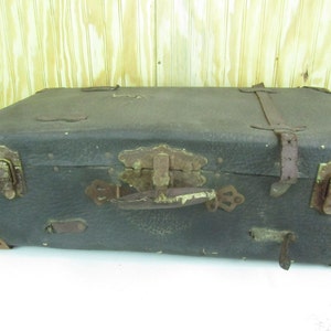 May include: A vintage, dark brown leather suitcase with brass hardware and leather straps. The suitcase has a worn and distressed look, with some scuffs and scratches on the surface. The suitcase has a handle on the top and two latches on the front.