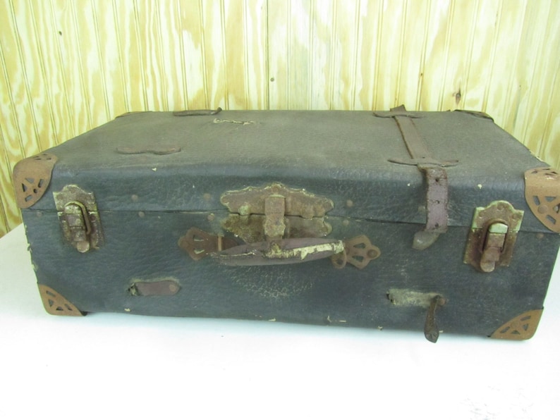 May include: A vintage, dark brown leather suitcase with brass hardware and leather straps. The suitcase has a worn and distressed look, with some scuffs and scratches on the surface. The suitcase has a handle on the top and two latches on the front.