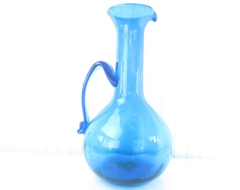 May include: A cobalt blue glass pitcher with a rounded body and a curved handle.