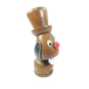 May include: A wooden figurine of a rabbit wearing a top hat. The rabbit has a red nose, black ears, and a white mouth. The figurine is brown with painted details.