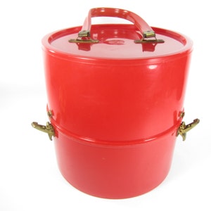 May include: A red plastic two-tiered storage container with a handle and gold-colored clasps.