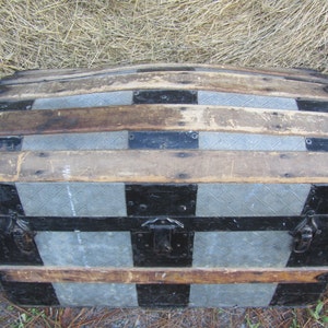 May include: A vintage wooden and metal travel trunk with a black and gray checkered pattern. The trunk has a rounded top and two metal handles.