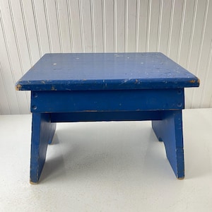 May include: A small, blue wooden stool with a simple design. The stool is made of solid wood and has a smooth, painted finish.
