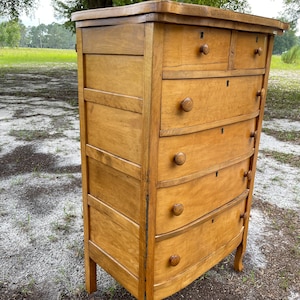Puede incluir: Una c&oacute;moda de madera vintage con seis cajones y bordes redondeados. La c&oacute;moda est&aacute; hecha de madera clara con un acabado natural. Tiene un dise&ntilde;o sencillo con peque&ntilde;os pomos redondos en cada caj&oacute;n.