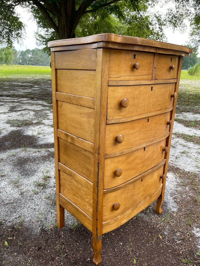 Puede incluir: Una c&oacute;moda de madera vintage con seis cajones y bordes redondeados. La c&oacute;moda est&aacute; hecha de madera clara con un acabado natural. Tiene un dise&ntilde;o sencillo con peque&ntilde;os pomos redondos en cada caj&oacute;n.