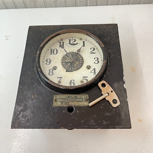 May include: A black metal clock with a white face and black numbers. The clock has a key for winding and the text "RELIANCE TIME SWITCH" on the bottom.