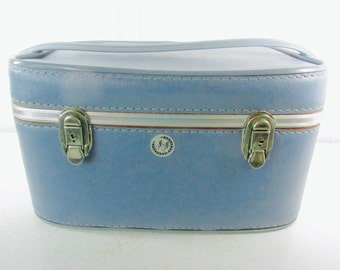 May include: A light blue vintage travel case with silver clasps and a white stripe. The case has a round logo with the letters "M & W" in the center.