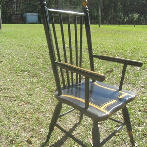 May include: Black wooden chair with a curved back, armrests, and a seat with yellow and black accents. The chair has a classic design and is set outdoors on a grassy lawn.