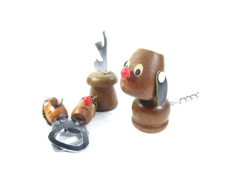May include: A collection of vintage wooden bottle openers and corkscrews. The set includes a dog-shaped corkscrew with a red nose and a metal corkscrew tail, and two other openers with cartoon faces.