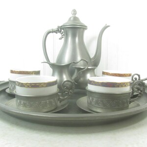 May include: A silver tea set with a teapot, creamer, sugar bowl, and four cups on a silver tray. The cups have a white base with a gold and purple trim.