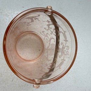 May include: A pink glass ice bucket with a floral design and a handle. The bucket is empty.