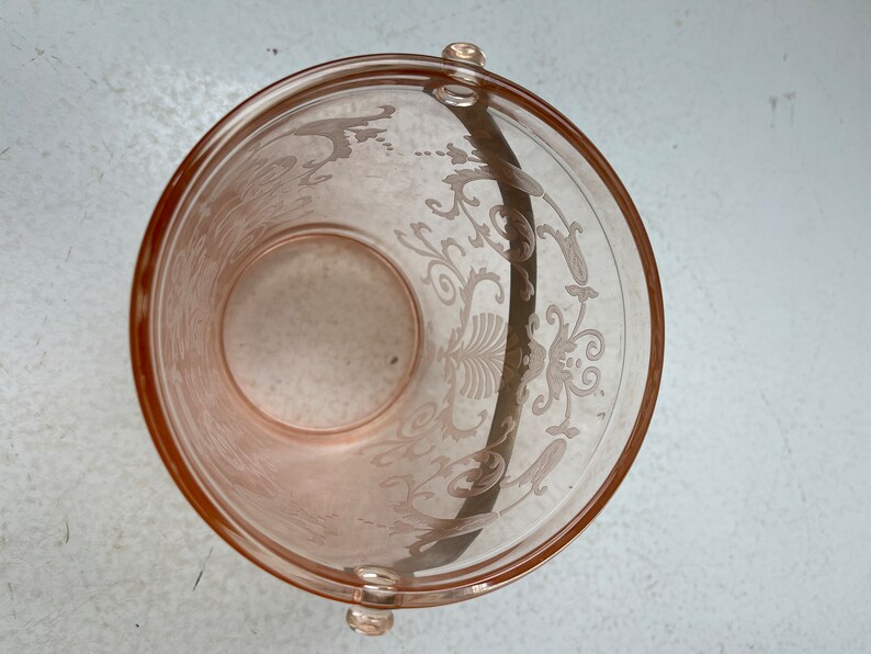 May include: A pink glass ice bucket with a floral design and a handle. The bucket is empty.