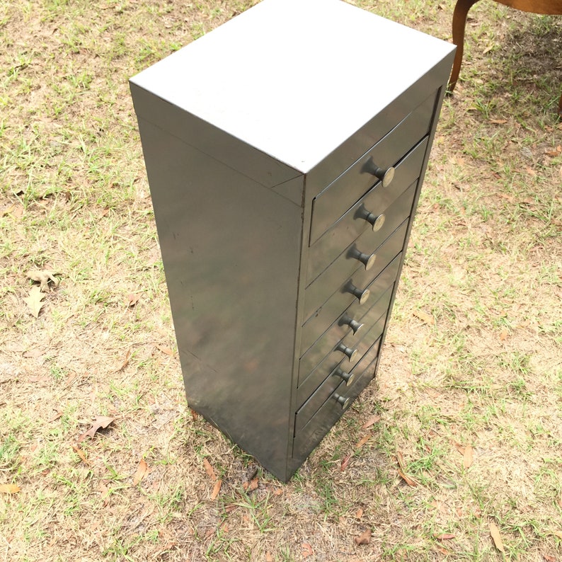 May include: A dark gray metal cabinet with eight drawers and silver knobs. The cabinet is standing on a grassy surface.