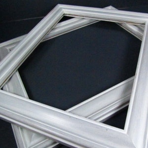 May include: Two white picture frames, one on top of the other, with a simple, slightly raised, decorative edge. The frames are made of wood and have a distressed, white paint finish.