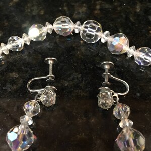 May include: A set of iridescent crystal earrings and a matching necklace. The earrings are clip-on style and feature a teardrop design with three crystal beads. The necklace is a strand of round crystal beads.
