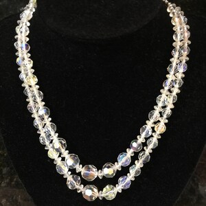 May include: A double strand necklace made of clear faceted crystal beads. The necklace is on a black velvet display stand.
