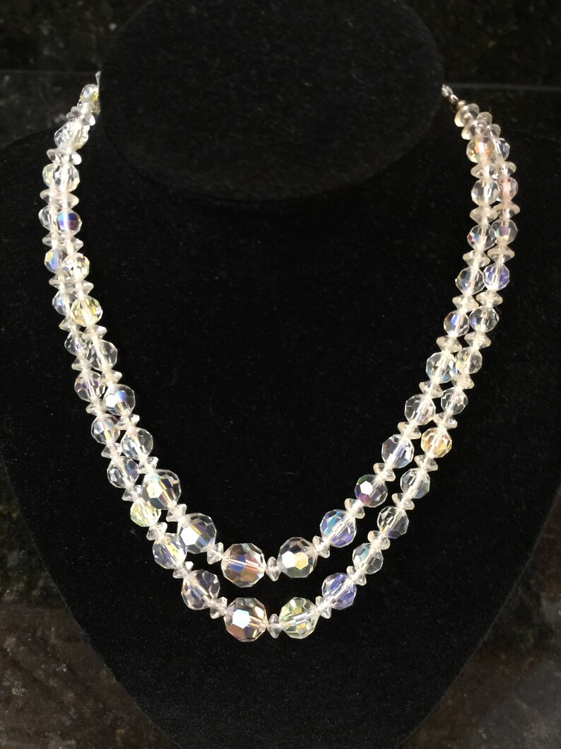 May include: A double strand necklace made of clear faceted crystal beads. The necklace is on a black velvet display stand.