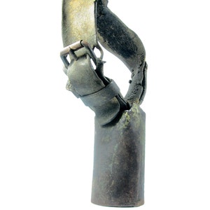 May include: A vintage cowbell with a leather strap and buckle. The bell is made of metal and has a dark green patina. The strap is brown leather and has a brass buckle.