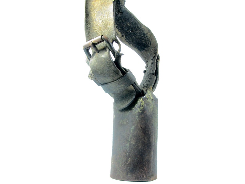 May include: A vintage cowbell with a leather strap and buckle. The bell is made of metal and has a dark green patina. The strap is brown leather and has a brass buckle.
