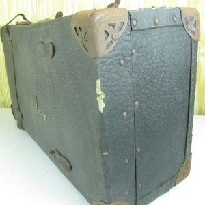 May include: A vintage, dark brown leather suitcase with metal accents and rivets. The suitcase has a worn and weathered appearance, suggesting it has been well-used over time.