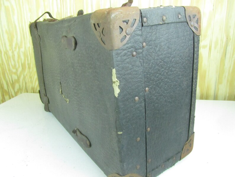 May include: A vintage, dark brown leather suitcase with metal accents and rivets. The suitcase has a worn and weathered appearance, suggesting it has been well-used over time.