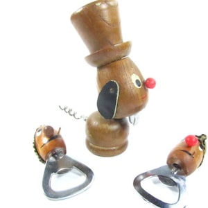 May include: A collection of wooden bottle openers and a corkscrew, all featuring a whimsical dog design. The dog-shaped items have brown bodies, black ears, red noses, and white eyes. The corkscrew dog wears a top hat.
