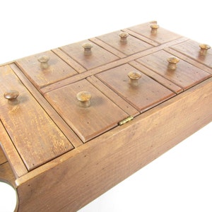 May include: A wooden box with 10 small drawers, each with a wooden knob. The box is made of light brown wood and has a slightly distressed finish.