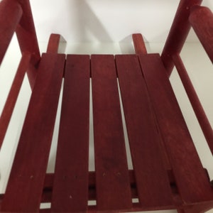 Puede incluir: Una silla mecedora de madera roja con un asiento de listones. La silla est&aacute; hecha de madera sin terminar y tiene un aspecto r&uacute;stico.