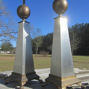 May include: A pair of silver and brass table lamps with a geometric design. The lamps have a round, brass top and a square base with decorative feet.