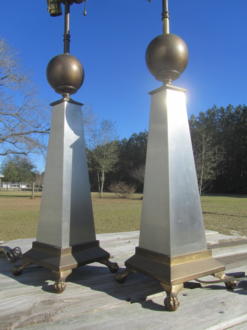 May include: A pair of silver and brass table lamps with a geometric design. The lamps have a round, brass top and a square base with decorative feet.