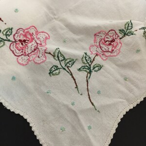 Op de afbeelding: Wit katoenen tafelkleed met een gehaakte rand en geborduurde roze rozen met groene bladeren.