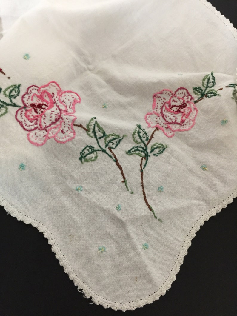 Op de afbeelding: Wit katoenen tafelkleed met een gehaakte rand en geborduurde roze rozen met groene bladeren.