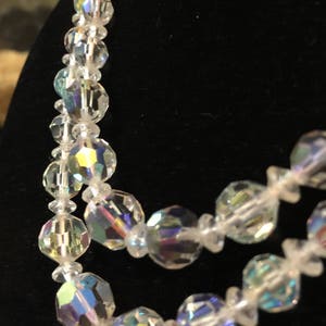 May include: A multi-strand necklace made of iridescent clear glass beads. The beads are faceted and have a rainbow sheen.