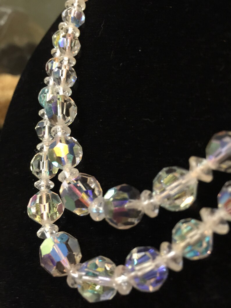 May include: A multi-strand necklace made of iridescent clear glass beads. The beads are faceted and have a rainbow sheen.