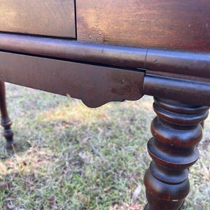 May include: A dark brown wooden table with a single drawer and turned legs. The table has a simple design and is in good condition.