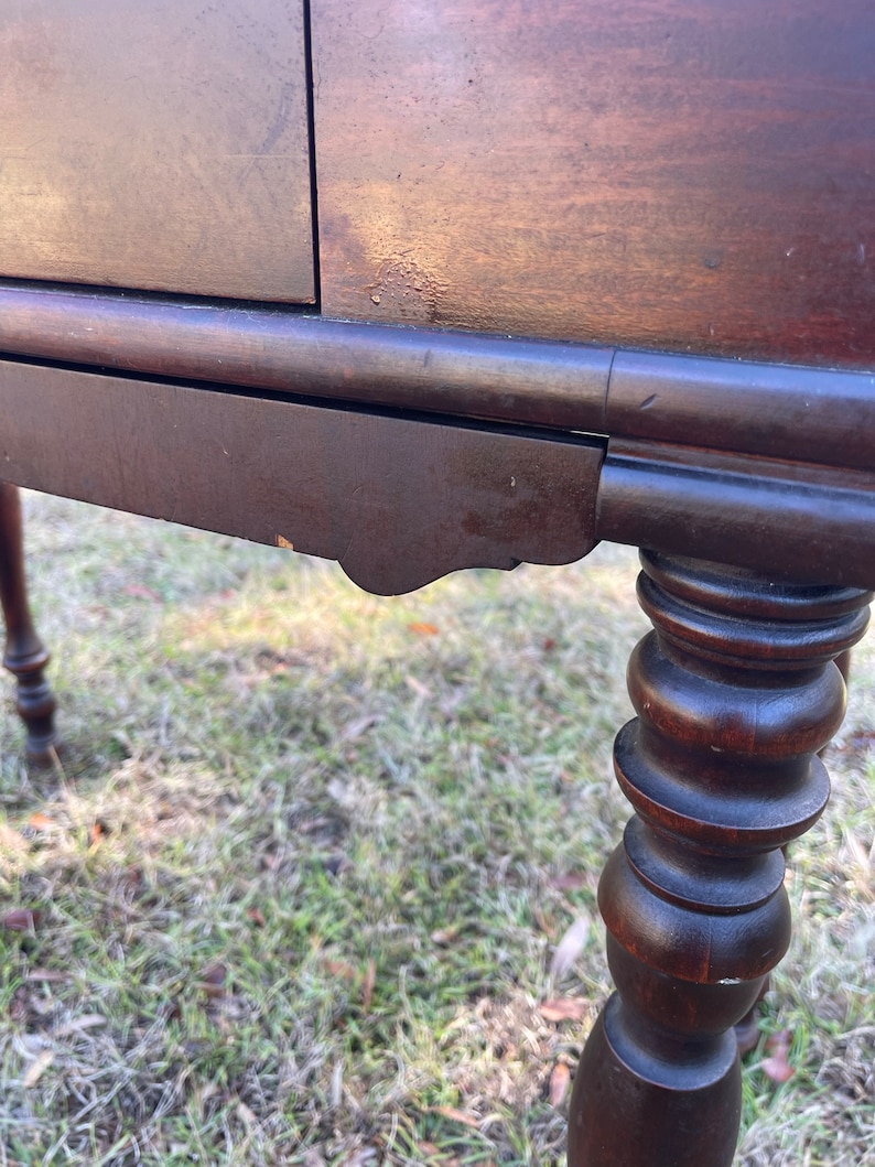 May include: A dark brown wooden table with a single drawer and turned legs. The table has a simple design and is in good condition.