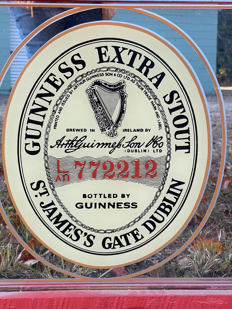 K&ouml;nnte beinhalten: Ein Vintage-Schild f&uuml;r Guinness Extra Stout mit einem goldenen und wei&szlig;en runden Design. Das Schild zeigt eine Harfe, den Text "Guinness Extra Stout" und die Worte "Brewed in Ireland by Arthur Guinness Son & Co Ltd as their trade mark and label".